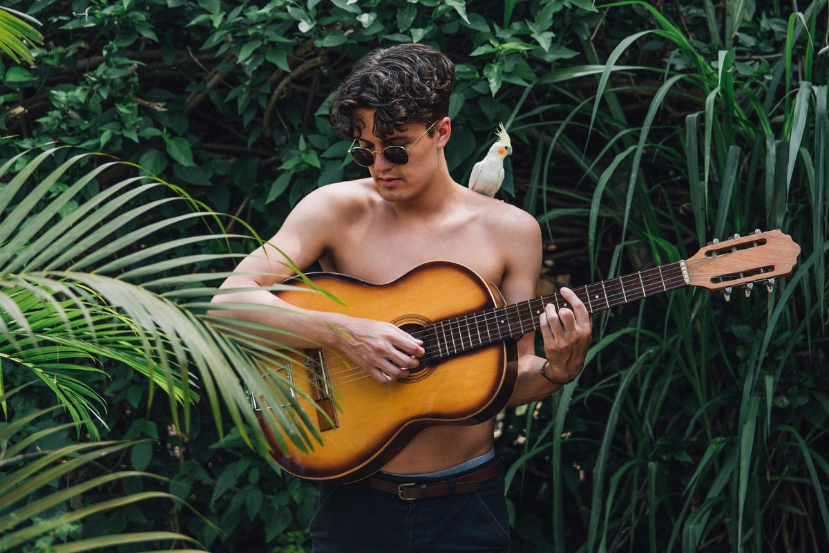 Emil Korkiakoski musico e compositor da banda younghearted em um ensaio em casa em que ele brinca com uma calopsita mansa nos ombros enquanto toca violão