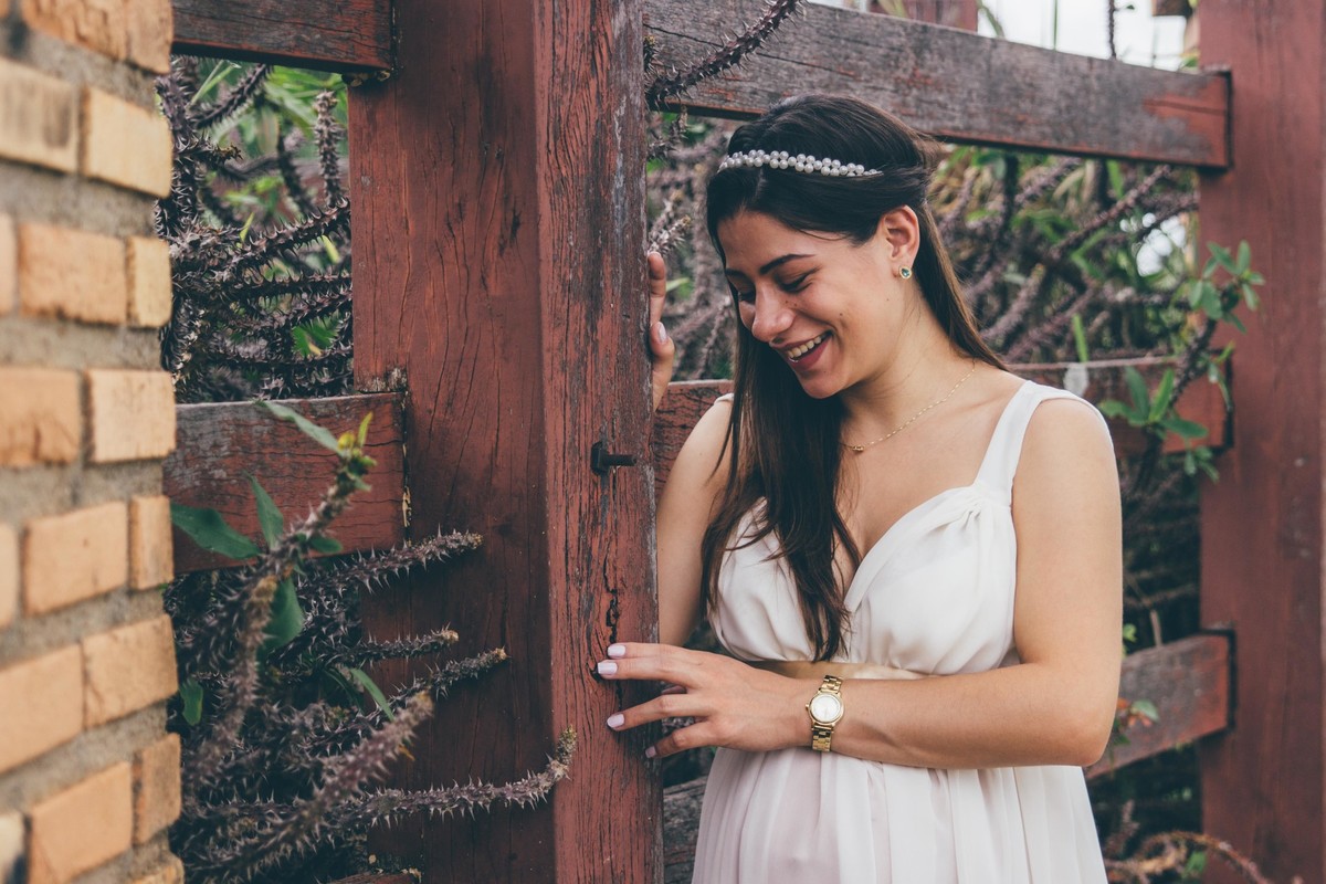 fotografia de gestante em que a mãe esta escorada em um muro de espinhos e sorrindo