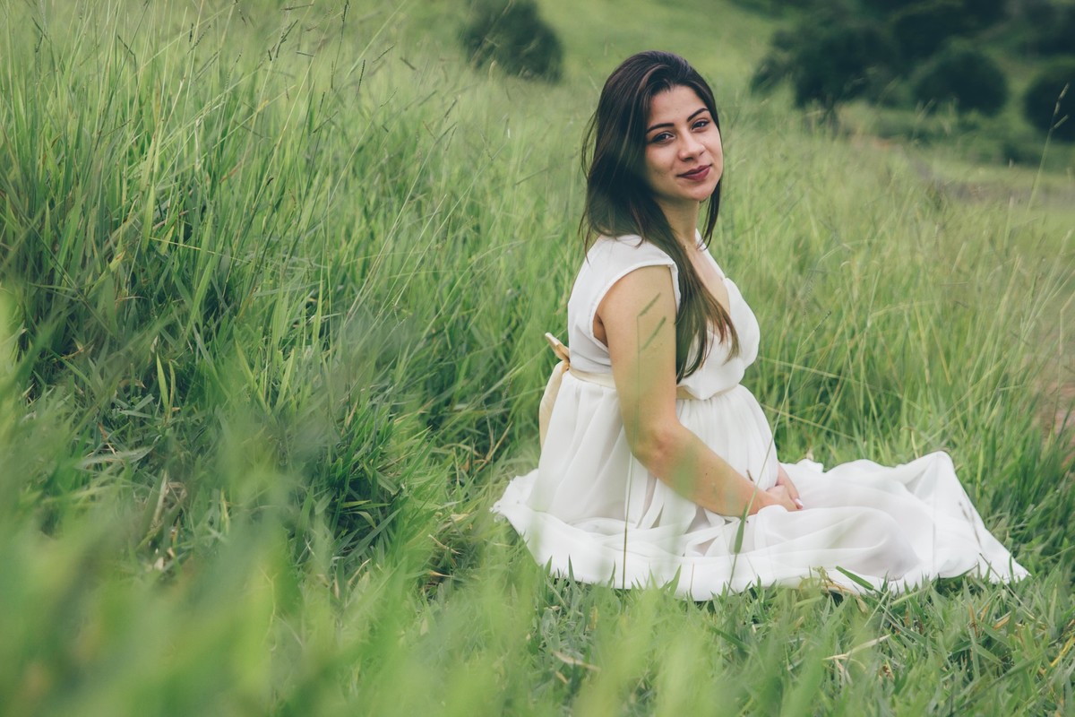 fotografia de gestante em que ela esta sentada na grama e olhando para o fotografo