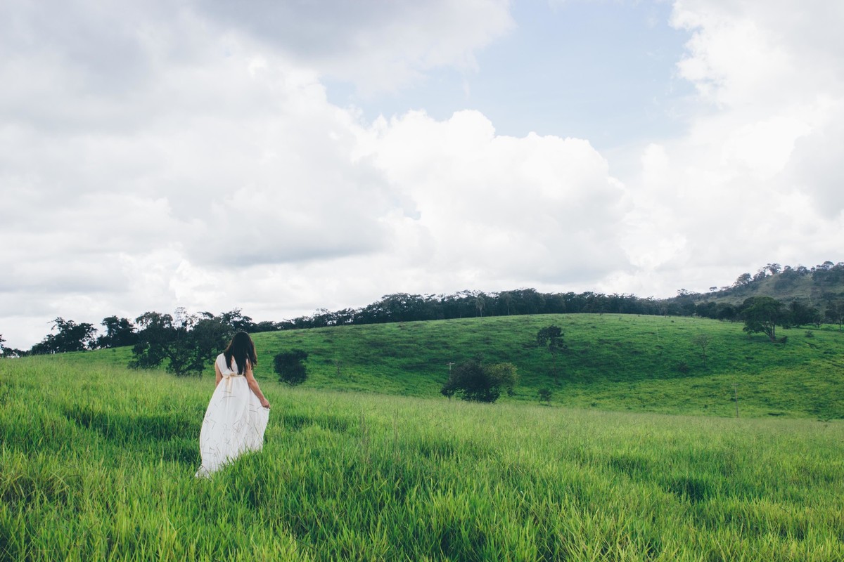 fotografia de gestante em que ela esta andando por um bosque verde usando um vestido branco