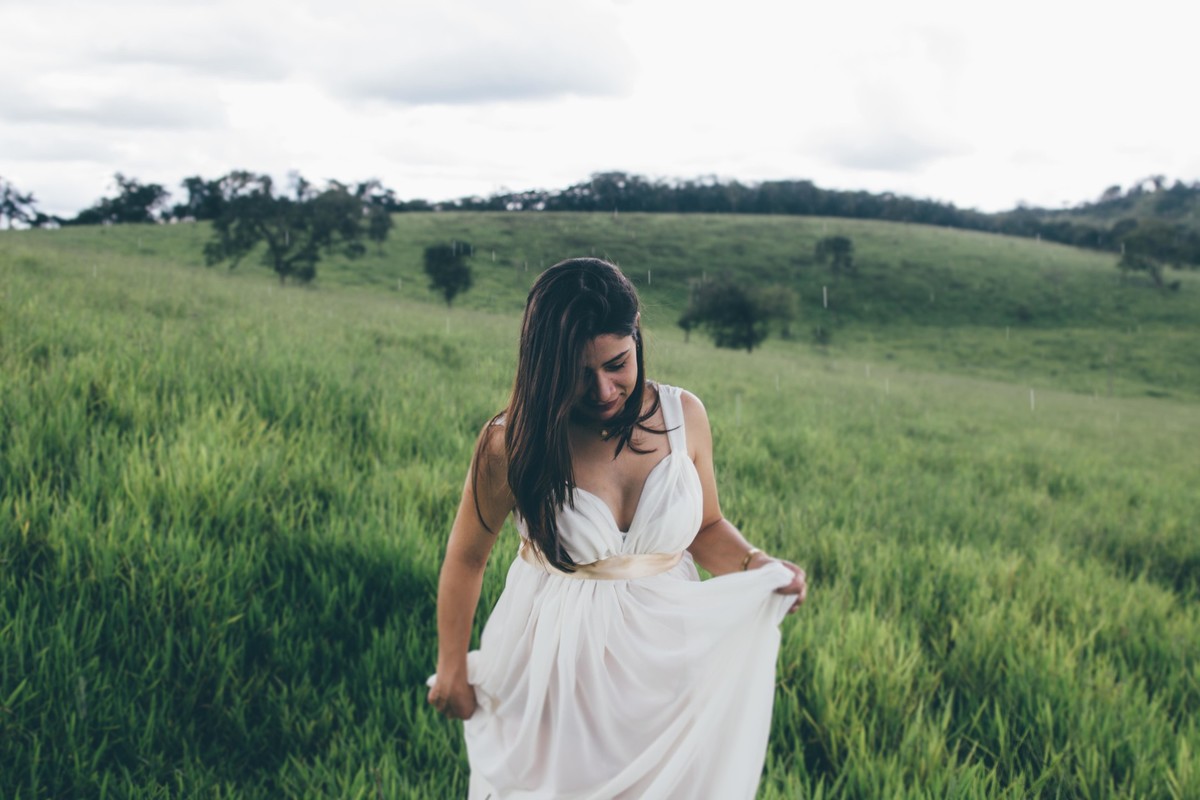 ensaio de gestante em que ela esta caminhando e olhando para baixo segurando seu vestido branco