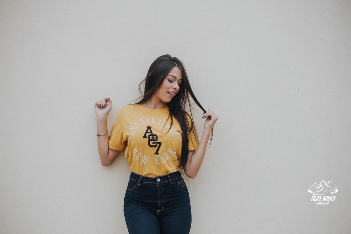 street fotografia em que a modelo esta encostada em uma parede branca e mexendo no cabelo