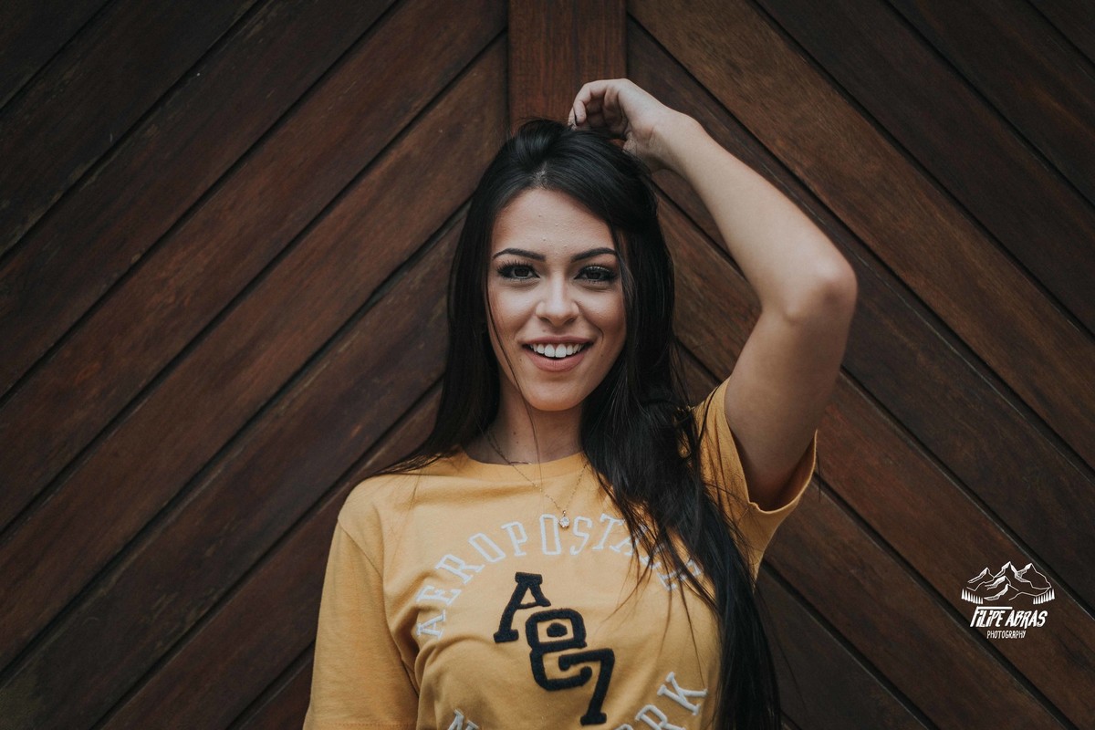 Retrato feminino da Livia Melo que segura seu cabelo e sorri para o fotografo profissional