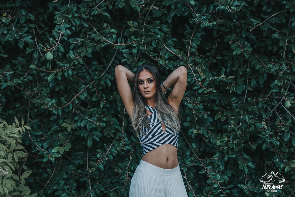 Retrato feminino em que a modelo esta na frente de um muro verde posando para a foto