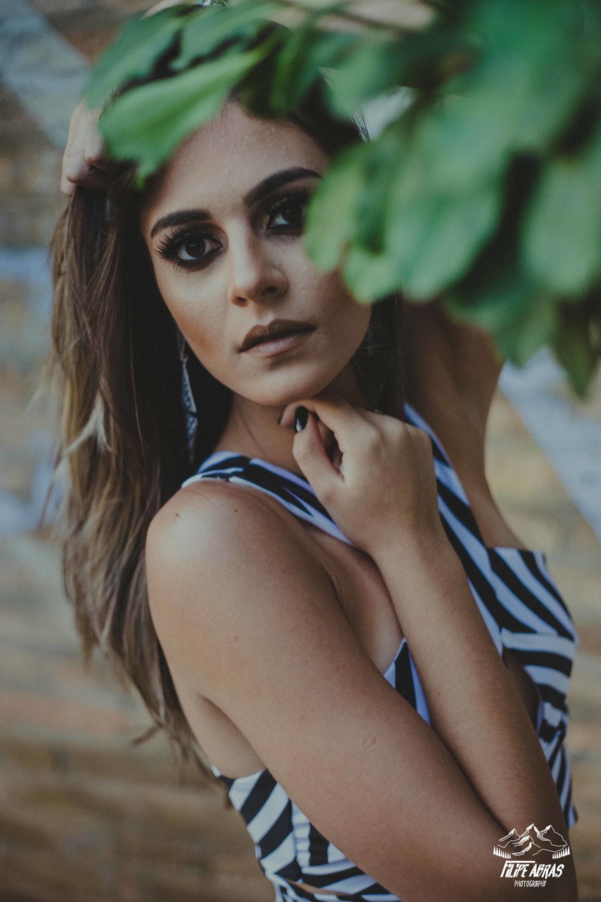 Retrato feminino em que a modelo esta olhando para a camera segurando o cabelo e com folhas na frente