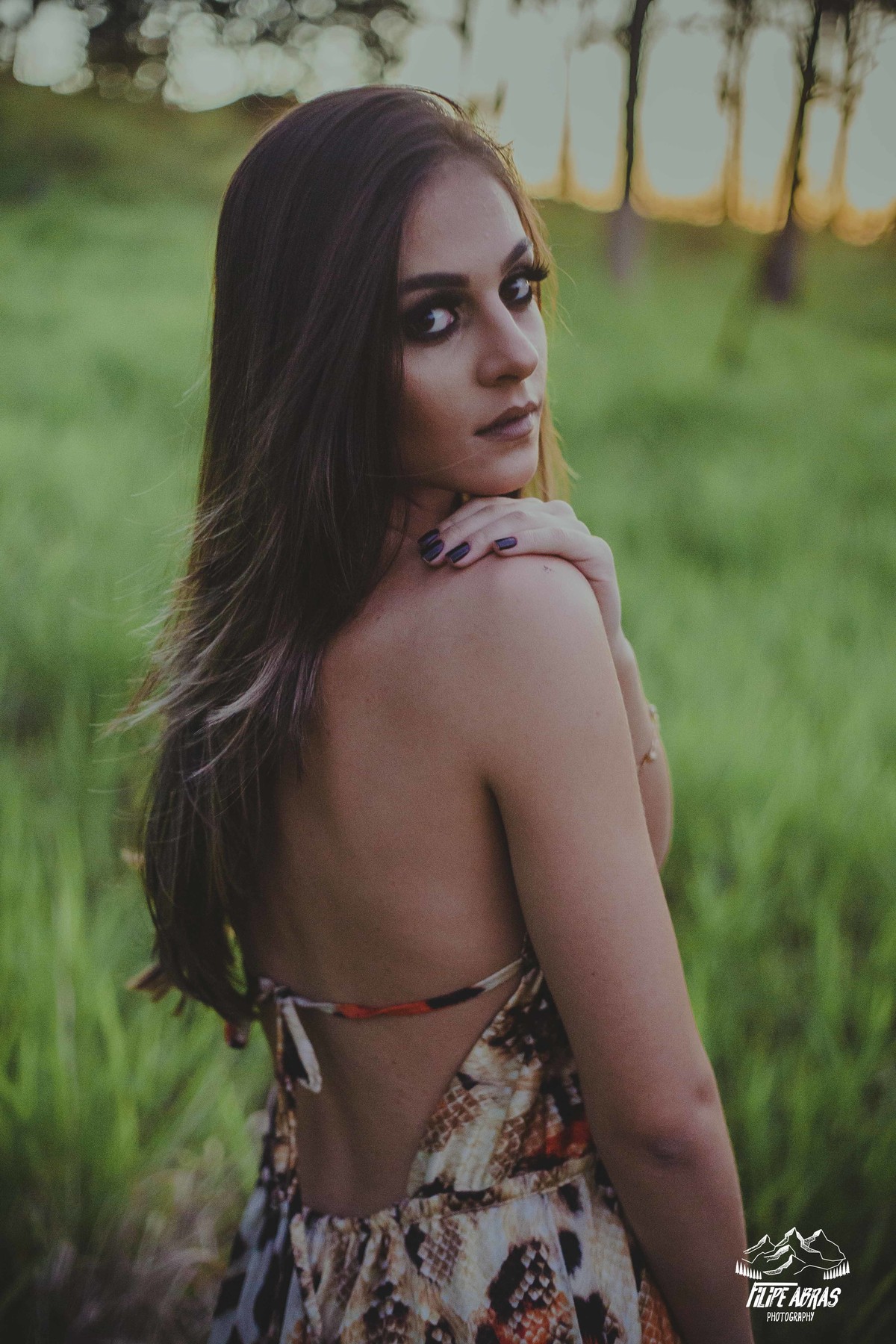 retrato feminino em que a modelo está olhando por cima dos ombros e encarando o fotografo em um ensaio no por do sol