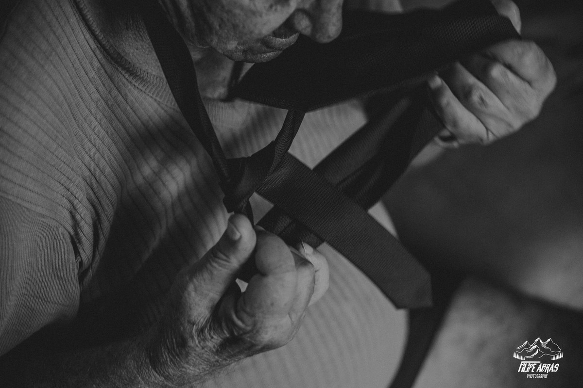 pai da noiva dando um nó na gravata sentado no sofá em uma fotografia de casamento em belo horizonte