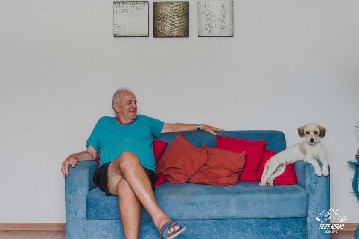 fotografia de make da noiva em que o pai da noiva esta sentado no sofá e sorrindo ao lado do cachorro da familia