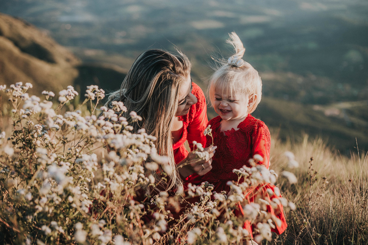 fotografia espontânea de familia em que a mãe está brincando com a filha no topo do mundo mg