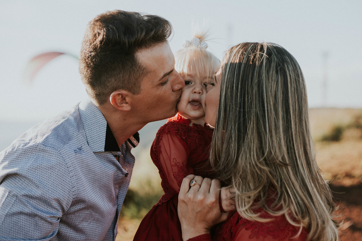 fotografia de familia em que os pais estão beijando o bebe no rosto ao mesmo tempo em uma fotografia criativa de ensaio de familia