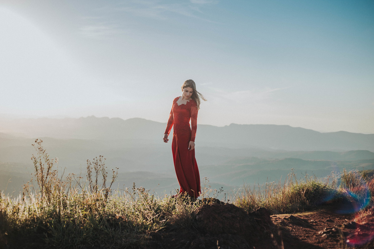 retrato feminino em que a modelo está usando um vestido vermelho no alto de uma montanha