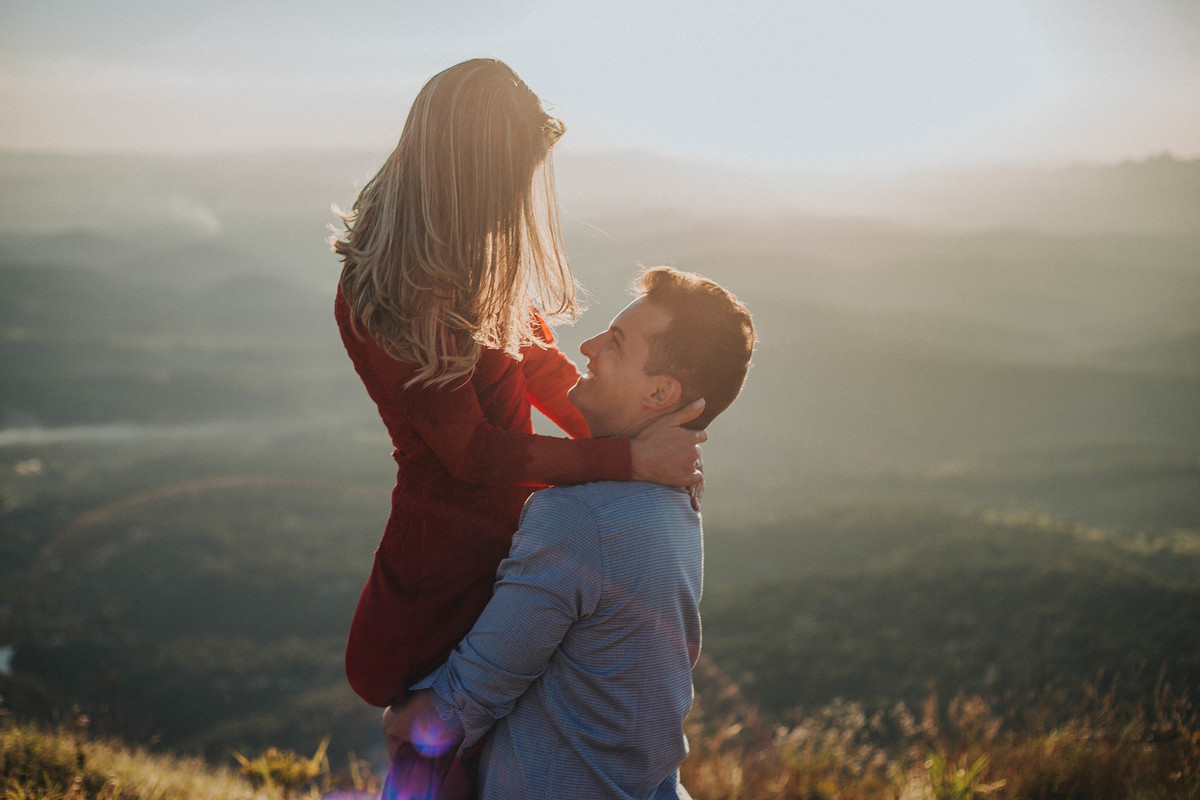 ensaio de pré casamento em que o noivo está carregando a noiva no colo enquanto um olha para o outro