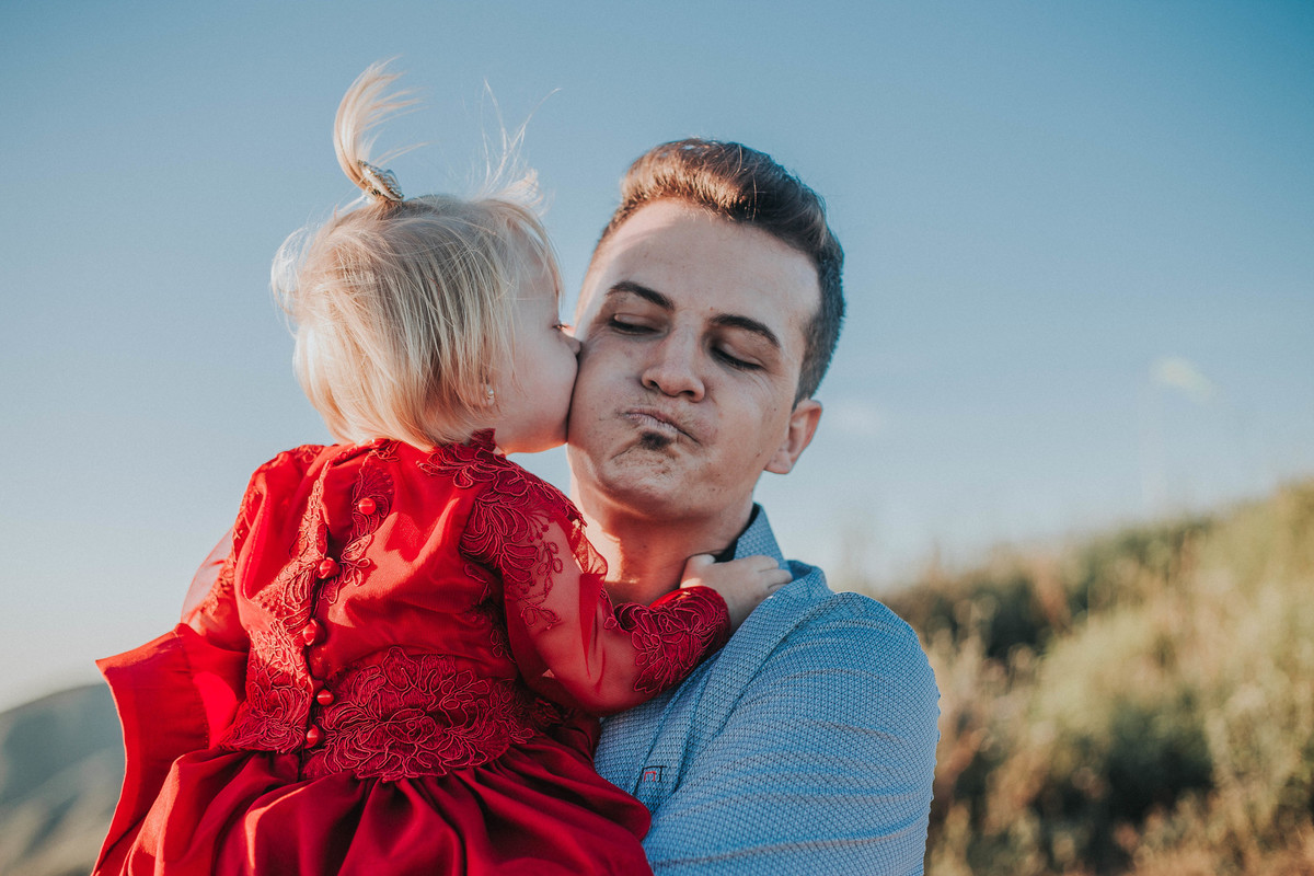 fotografia de pai e filha em que a filha está beijando a bochecha do pai