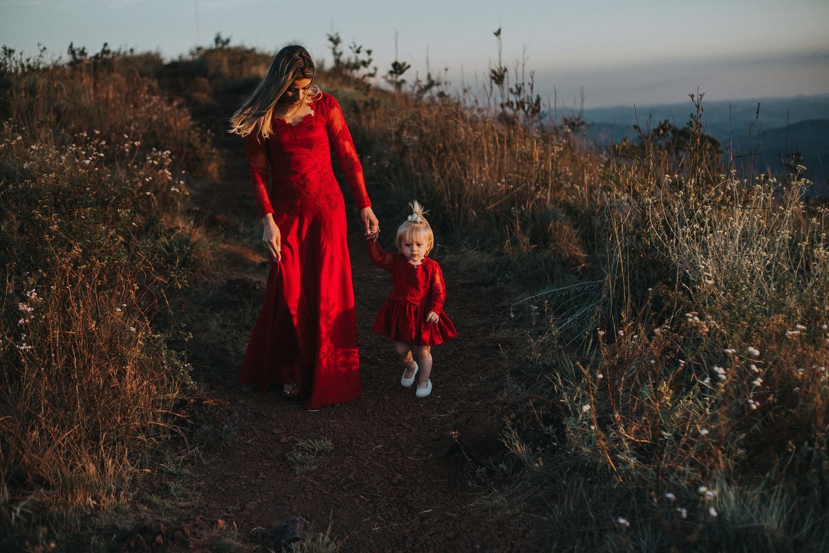 retrato de familia em que a mãe e a filha tem o mesmo vestido vermelho e caminhão de mãos dadas no topo do mundo