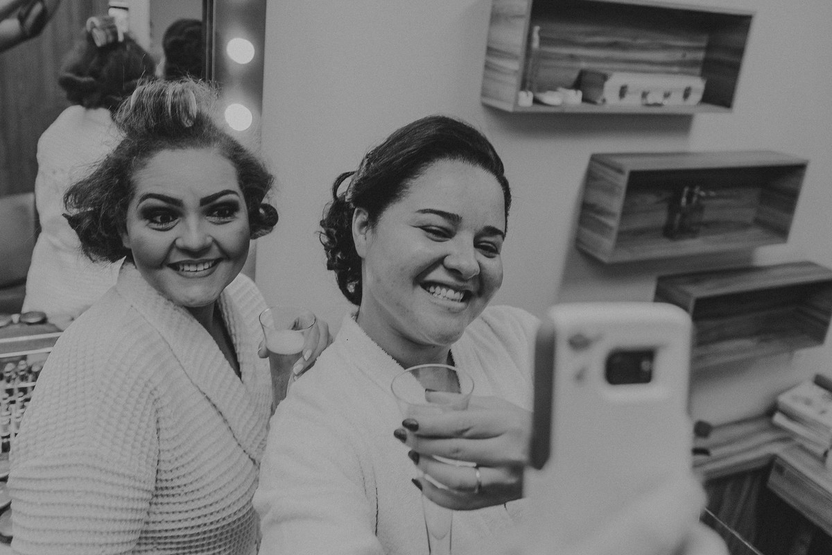 Noiva e madrinha sorrindo e tirando uma selfie durante o making of da noiva
