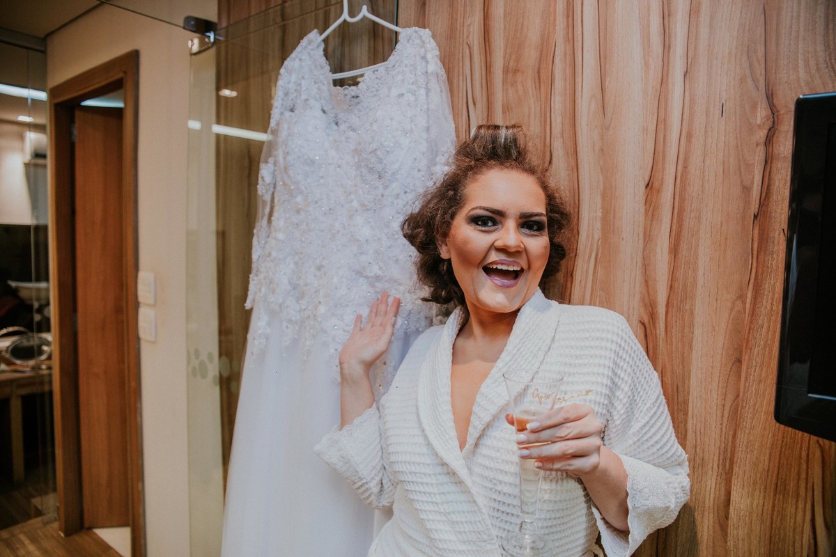 noiva sorrindo ao lado do seu vestido de casamento