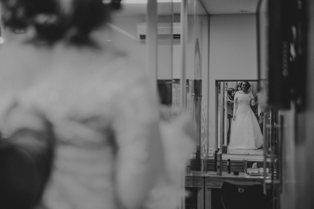 noiva se vendo no espelho enquanto acabam de fechar seu vestido