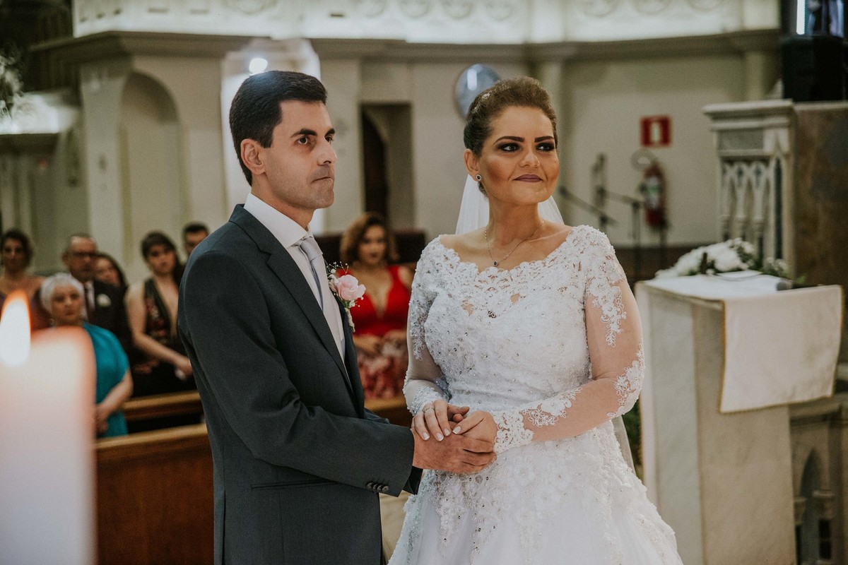 noivos de mãos dadas e olhando para o padre