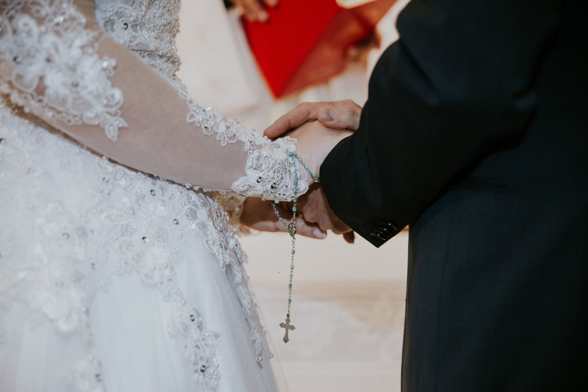 Detalhes de casamento em que a noiva carrega um terço em suas mãos