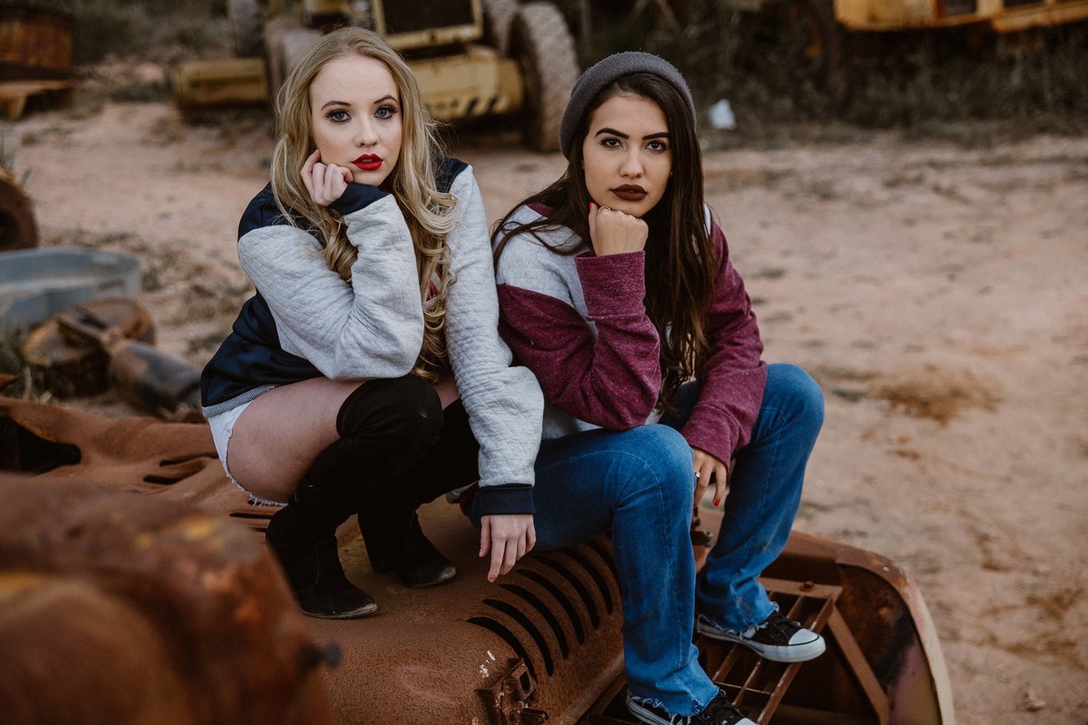 book feminino entre amigas em que estão sentadas encima de um carro abandonado