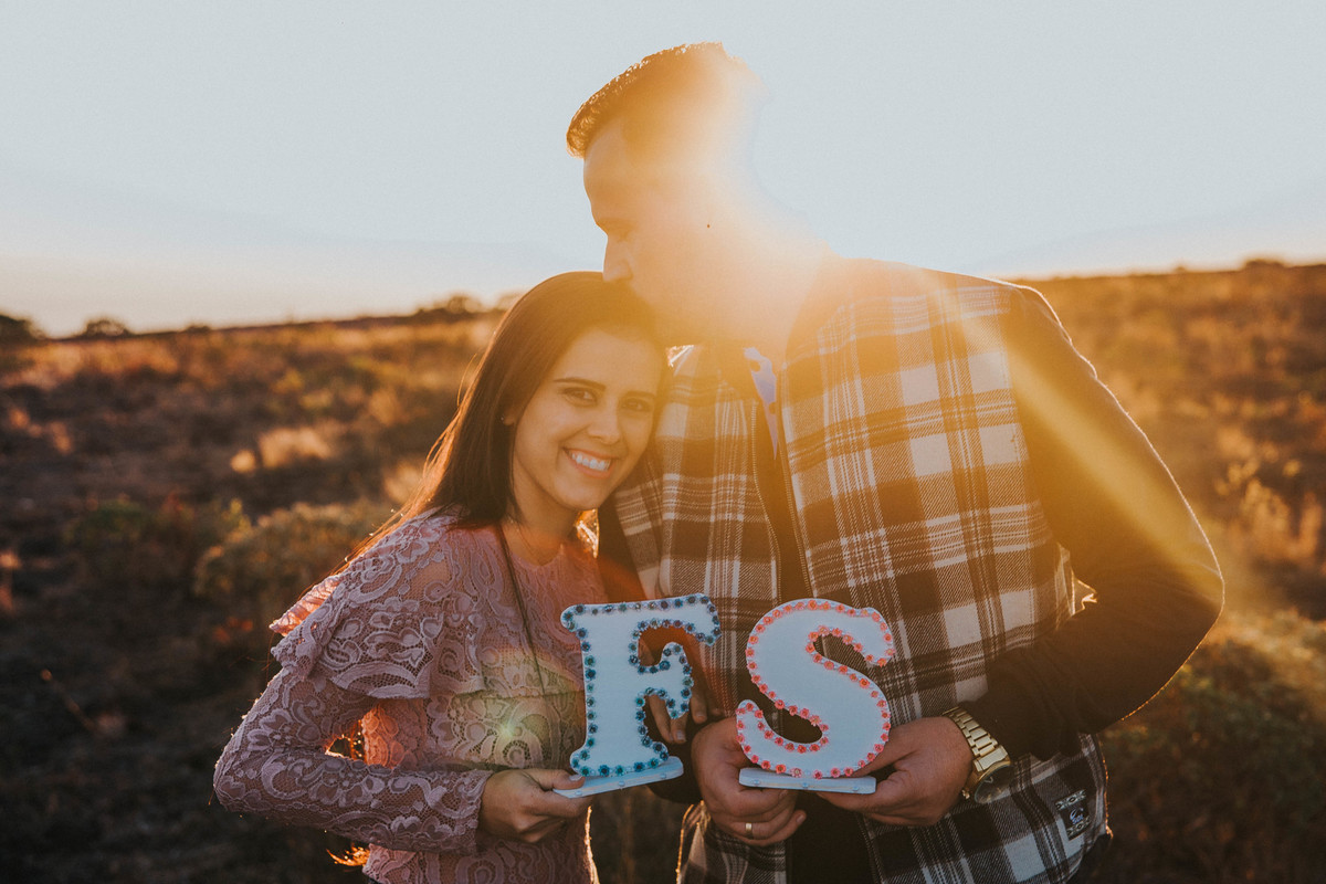 Noivos no por do sol com uma plaquinha com as iniciais dos dois