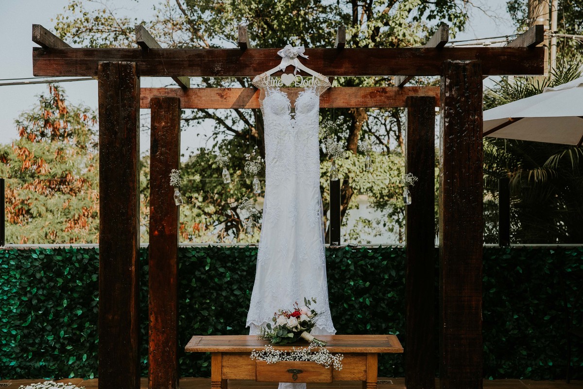 vestido de noiva pendurado no local da cerimonia perto um buque em uma inpração para vestido de noiva