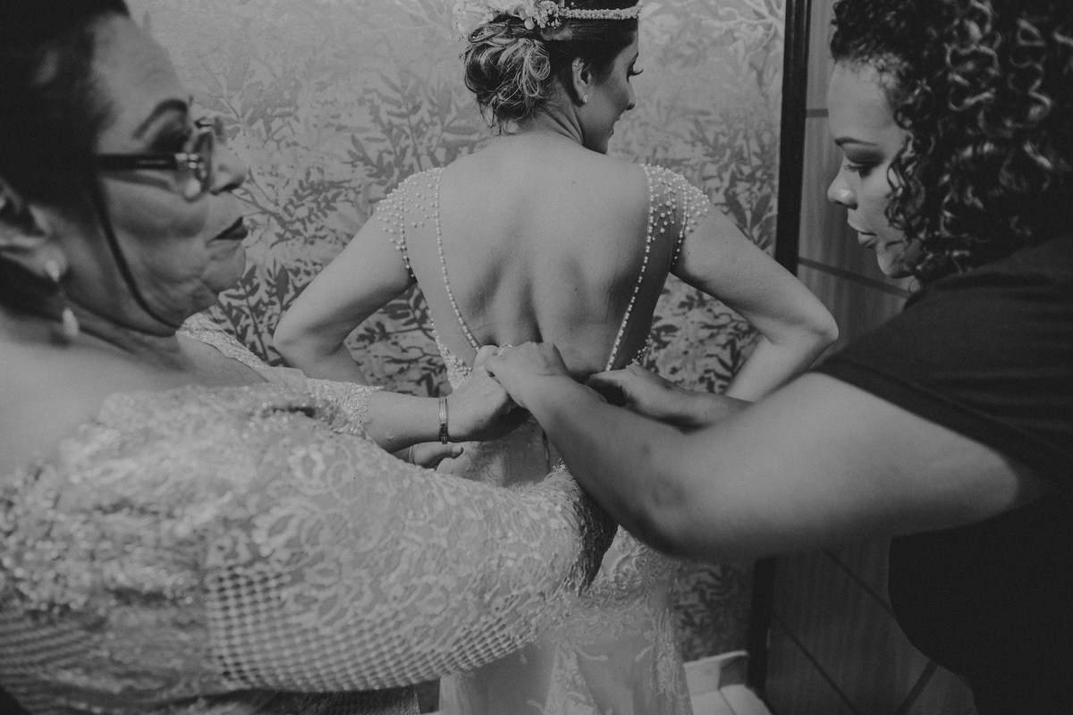 Mãe da noiva e maquiadora ajudando a noiva a vestir o vestido de casamento dos sonhos