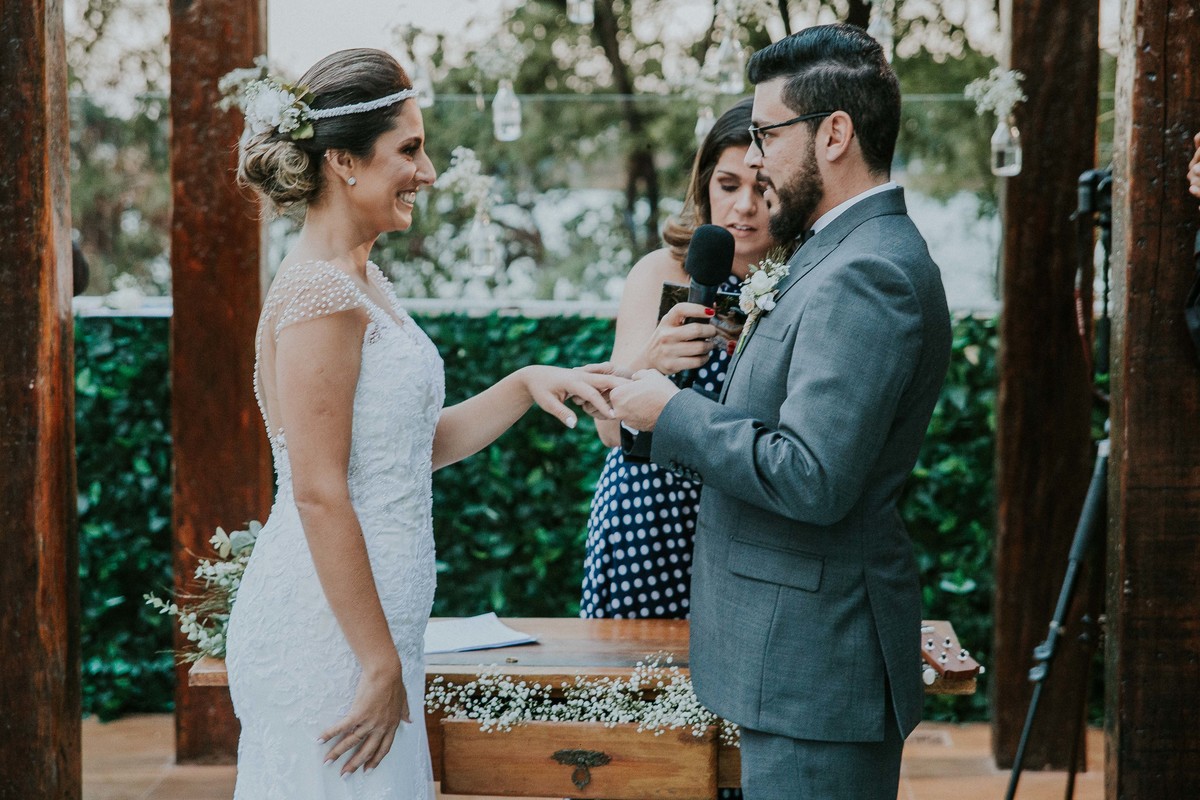 Troca de alianças em que o noivo esta  sorrindo para a noiva