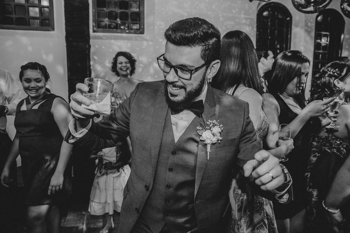 Noivo dançando com o copo de bebida na mão e sorrindo durante a recepção de casamento em bh