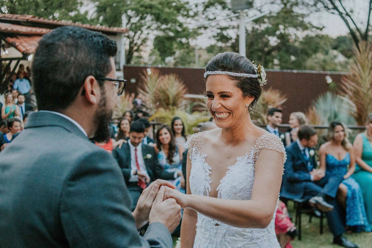 noivo colocando a aliança nos dedos da noiva enquanto ela sorri