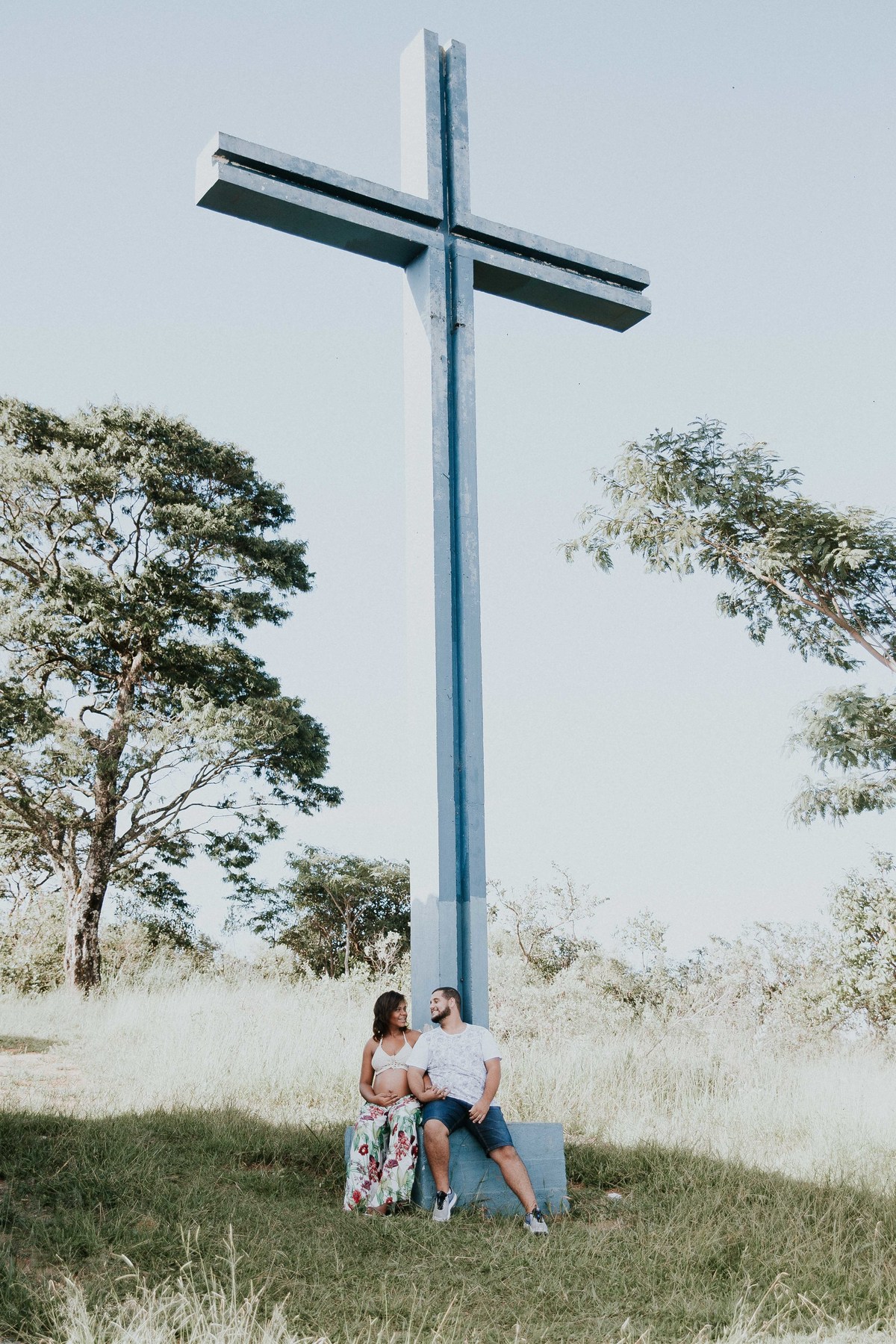 inspiração para ensaio de gestante no qual o casal está em baixo de uma cruz.