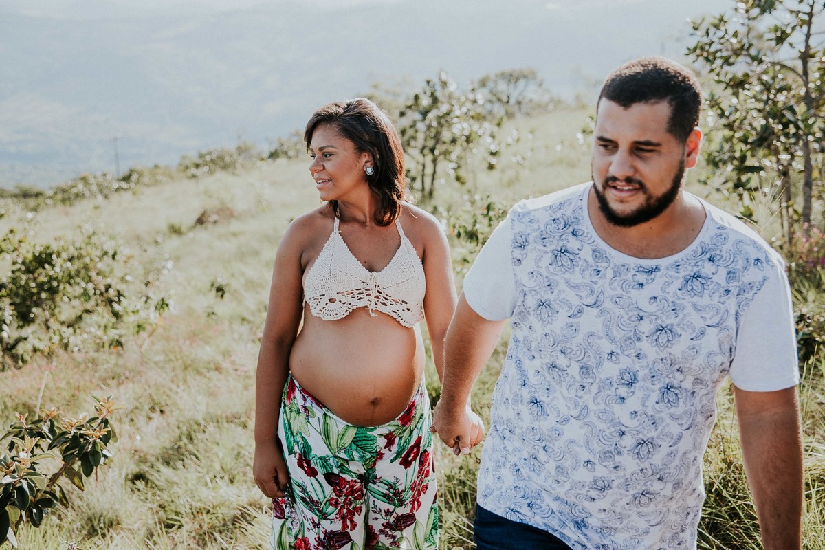 fotografia criativa de gestante no qual os pais estão caminhando no alto da montanha
