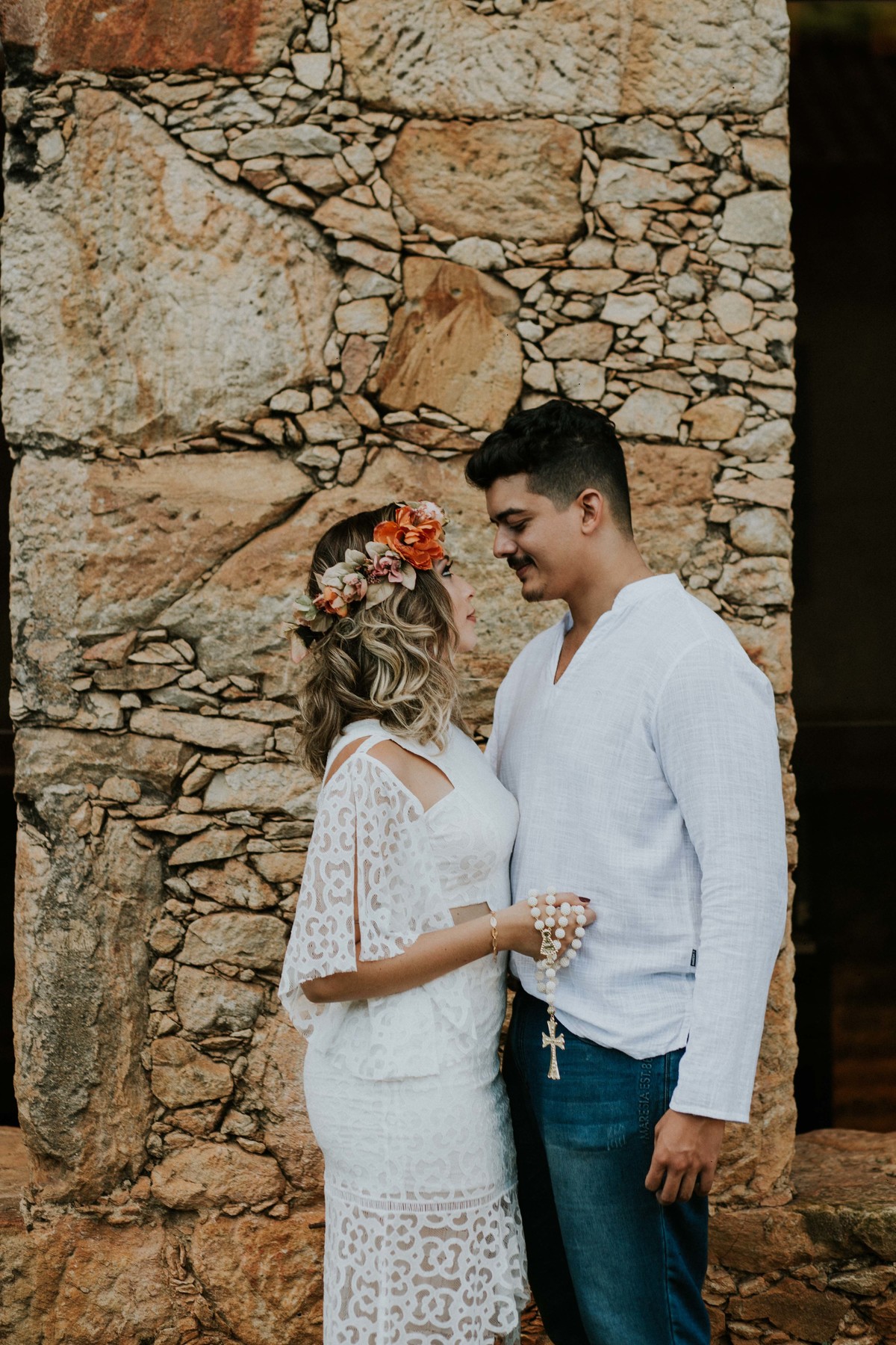 ensaio de pré casamento na serra do caraça no qual os noivos estão de branco e segurando um terço