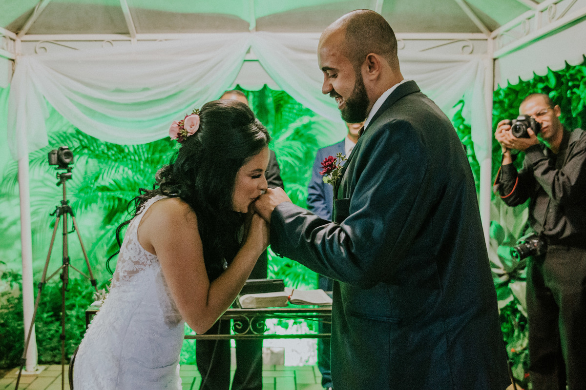 noiva beijando a mão do noivo após colocar a aliança de casamento no dedo dele