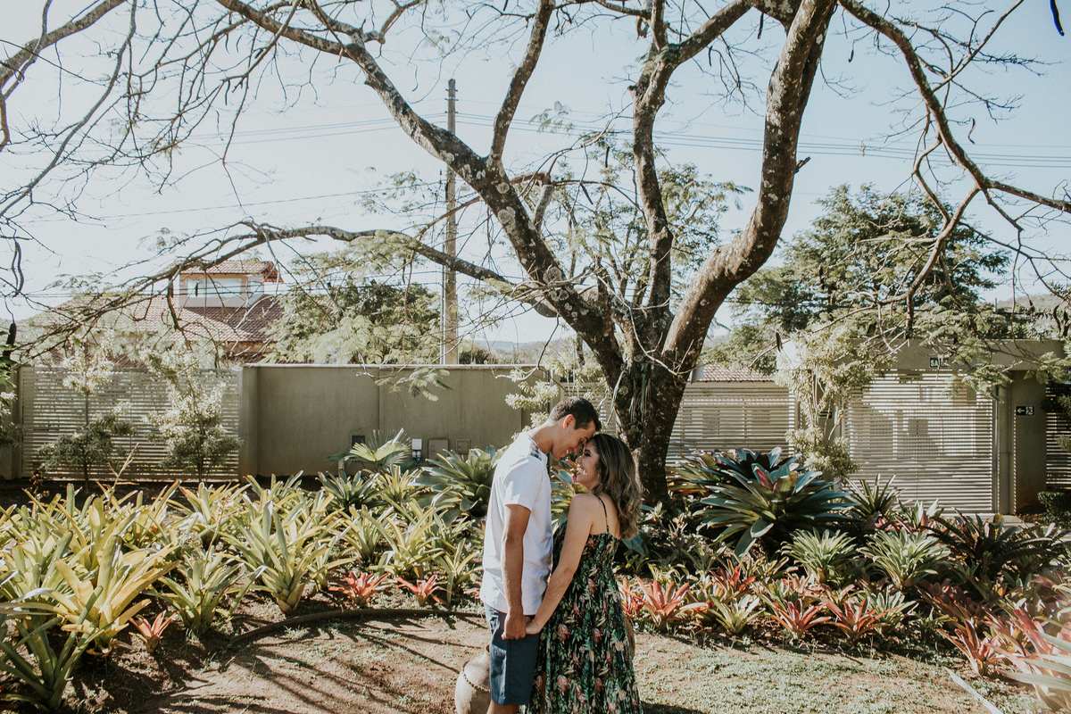 foto criativa de casal no qual os dois estão com a cabeça colada e em baixo de uma arvore em um lindo jardim
