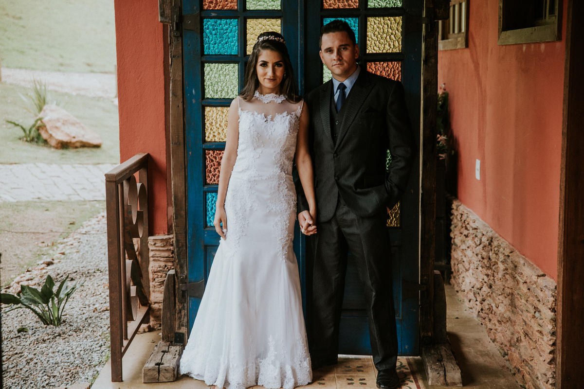 Fotografia de pós casamento rustico no qual os noivos estão de mãos dadas na frente de uma porta de vidro para a entrada da noiva na fazenda arraial velho