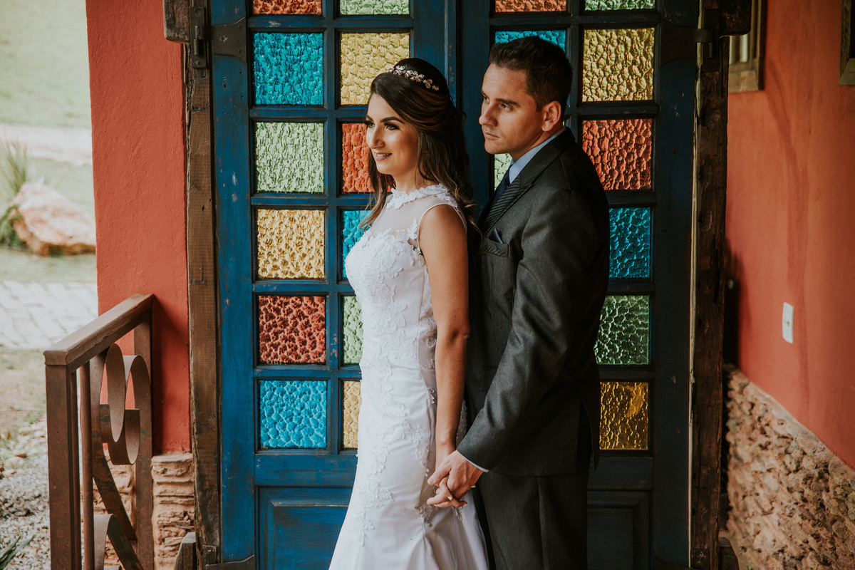 Fotografia de pós casamento rustico no qual os noivos estão de mãos dadas na frente de uma porta de vidro para a entrada da noiva na fazenda arraial velho