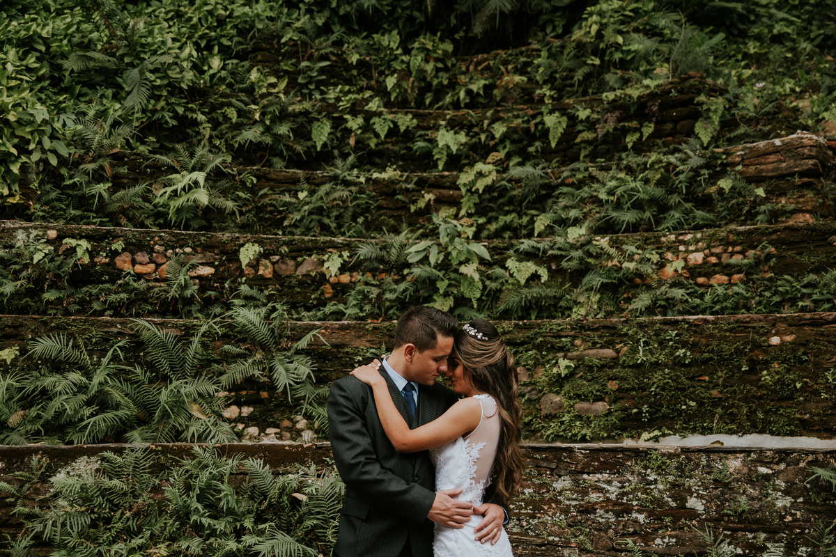 Fotografia de pós casamento na fazenda arraial velho no qual os noivos estão se abraçando em frente a um muro de pedras rustico 