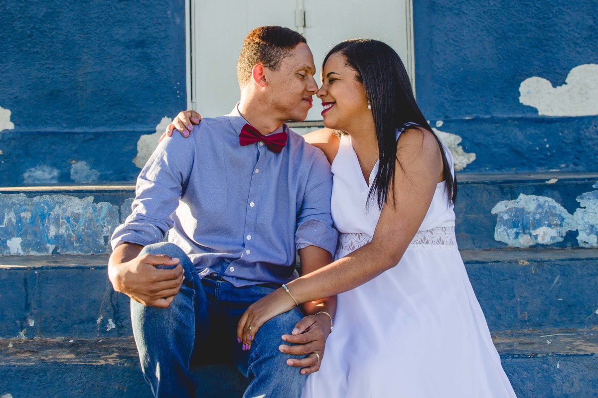 fotos no por do sol de recem casados, na frente de uma igreja azul, noiva com vestido branco e o noivo com blusa social e gravata borboleta