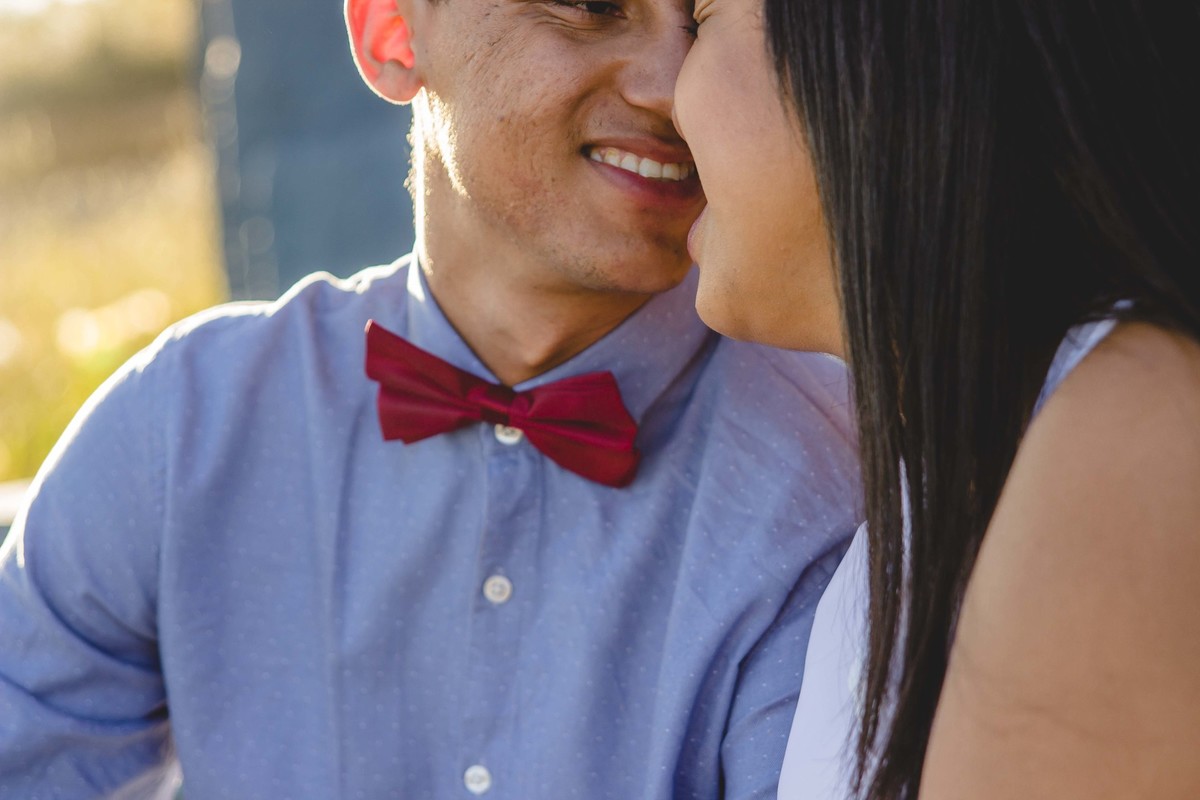 fotos no por do sol de recem casados, na frente de uma igreja azul, noiva com vestido branco e o noivo com blusa social e gravata borboleta