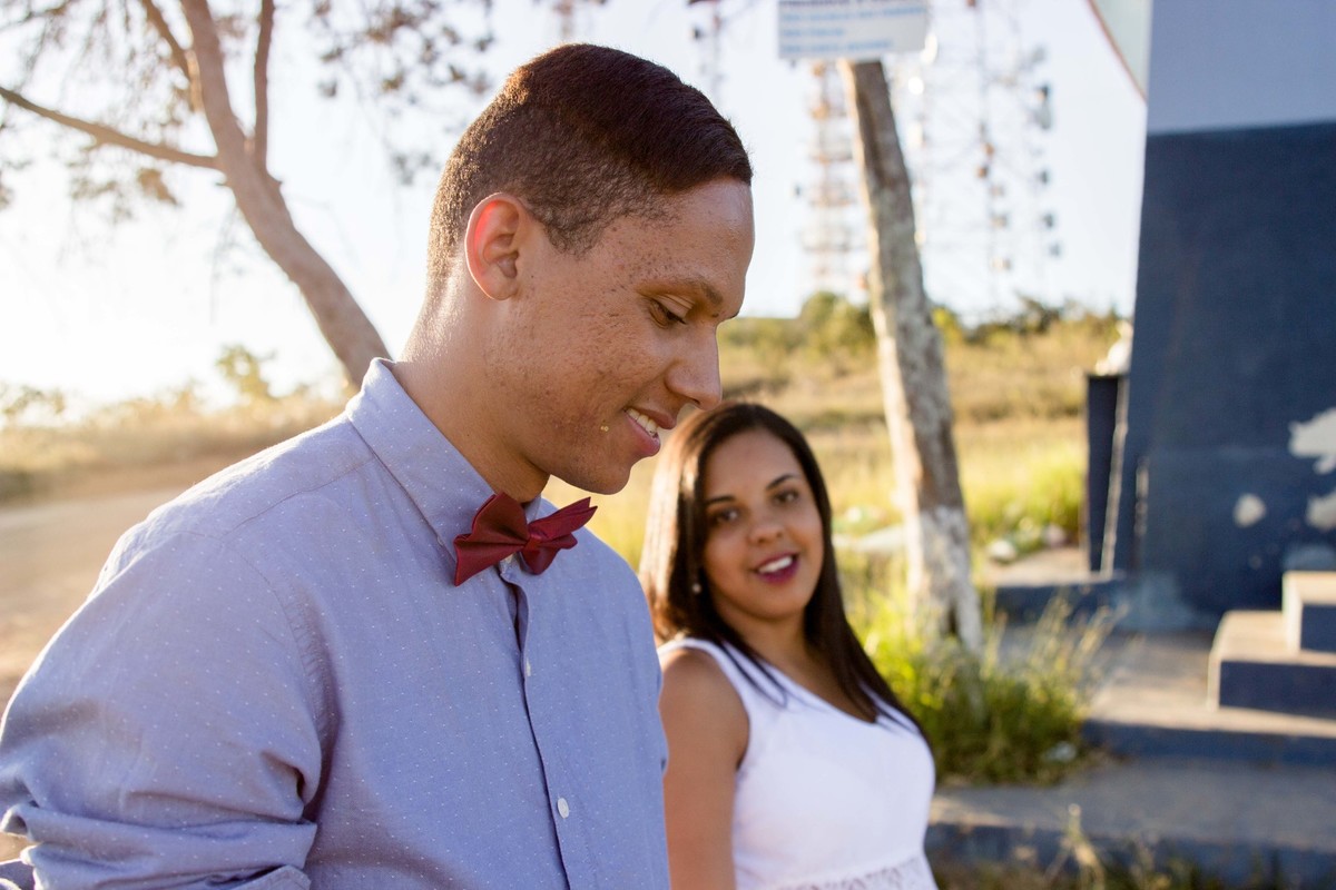 fotos no por do sol de recem casados, na frente de uma igreja azul, noiva com vestido branco e o noivo com blusa social e gravata borboleta