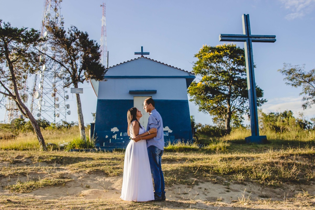 fotos no por do sol de recem casados, eles estão sorrindo e abraçados olhando um para o outro com um olhar apaixonado, na frente de uma igreja no alto da montanha, uma igreja azul antiga e bonita