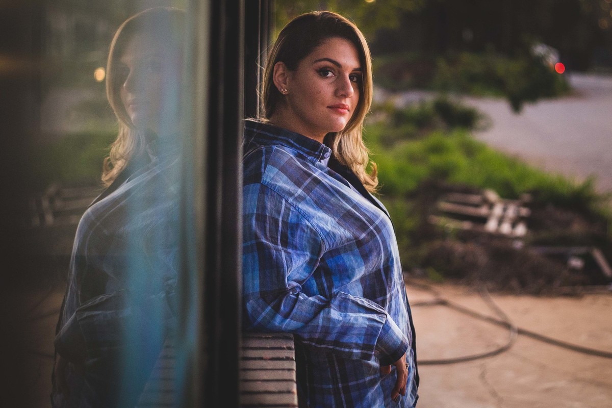 Ensaio fotografico no por do sol, mulher usando roupas masculinas e aboatoando a camisa, fotos feitas em Juatuba em posto abandonado, bluxa xadrez azul da uma ideia de como olhar para a camera em um ensaio