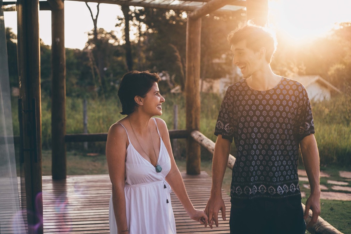 casal sorrindo e se olhando de mão dadas na varanda de casa no por do sol