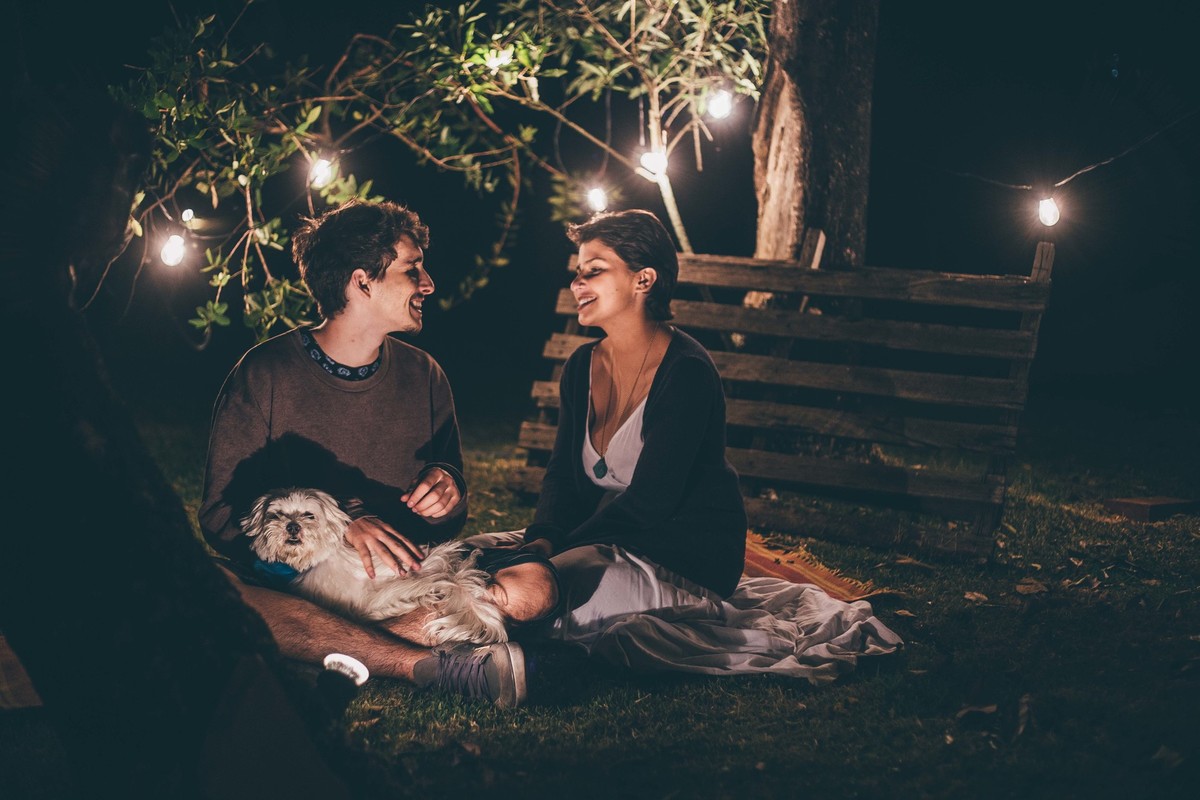 Foto de casal a noite com varal de luz, casal se olhando e sorrindo