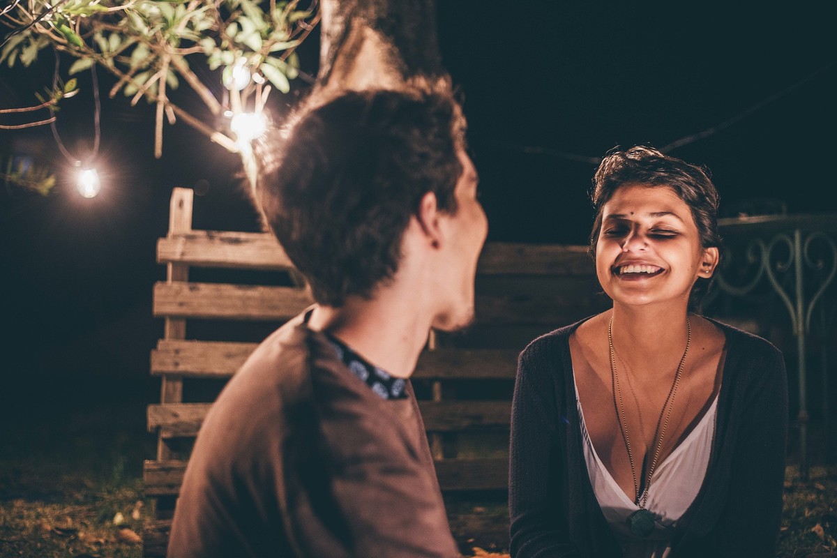 Foto de casal a noite com varal de luz, casal se olhando e rindo