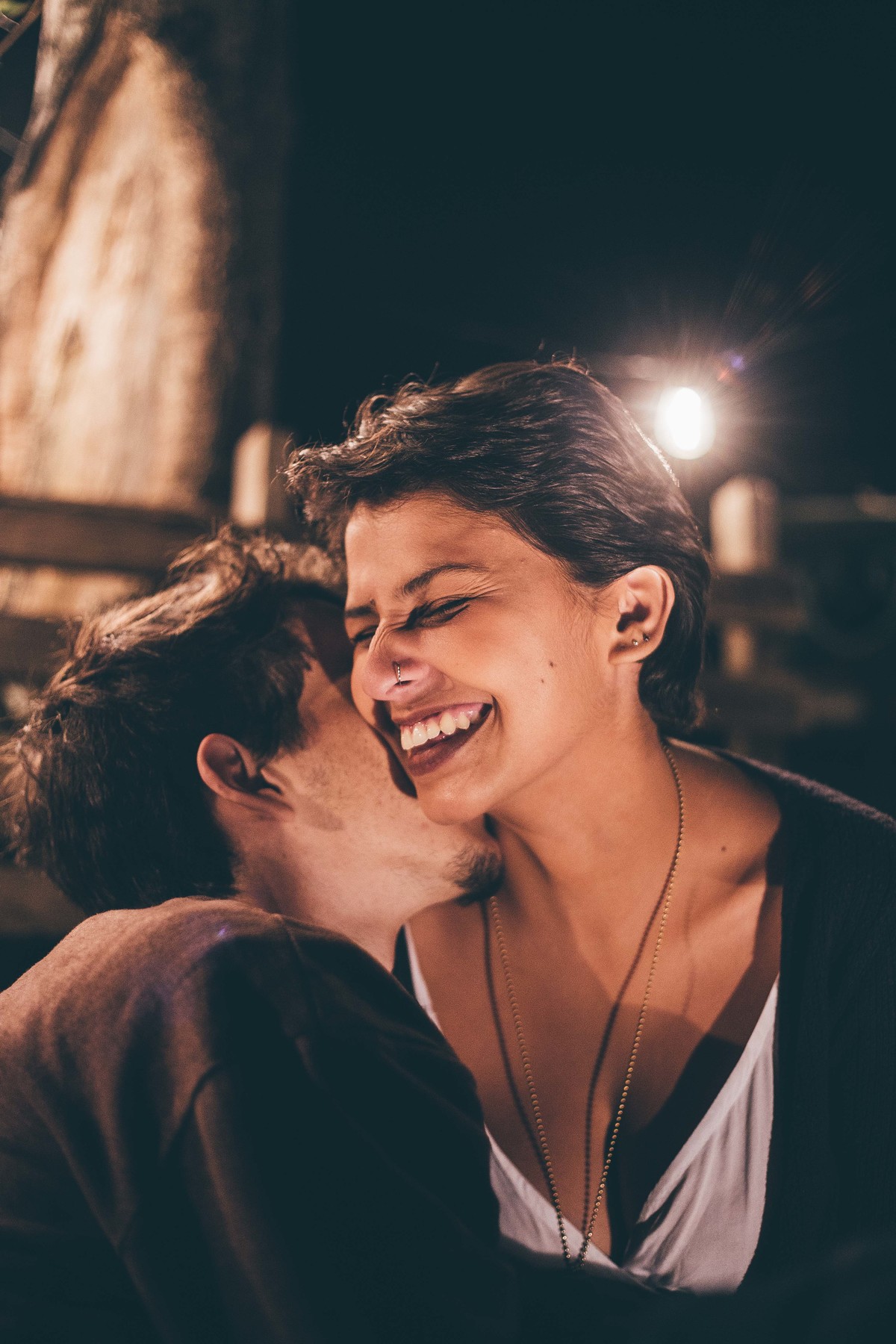 Foto de casal a noite com varal de luz, casal fazendo carinho um no outro e sorrindo