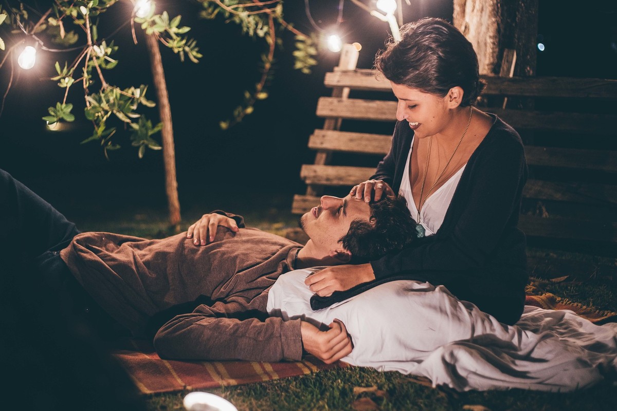 Foto de casal a noite com varal de luz, casal fazendo carinho um no outro e sorrindo
