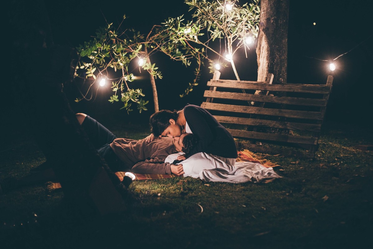 Foto de casal a noite com varal de luz, homem deitado no colo da namorada