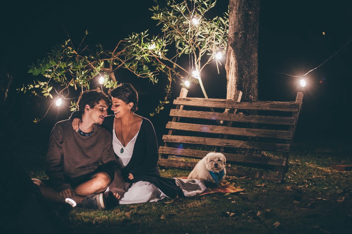 Foto de casal a noite com varal de luz, casal fazendo carinho um no outro e sorrindo